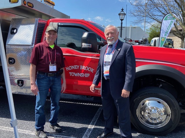Two men stand beside a red fire truck labeled "Honey Brook Township" at an outdoor event