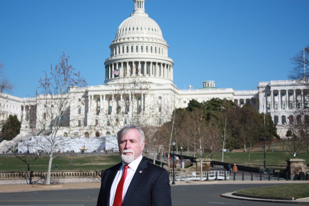 A man in a suit stands confidently in front of the U.S. Capitol